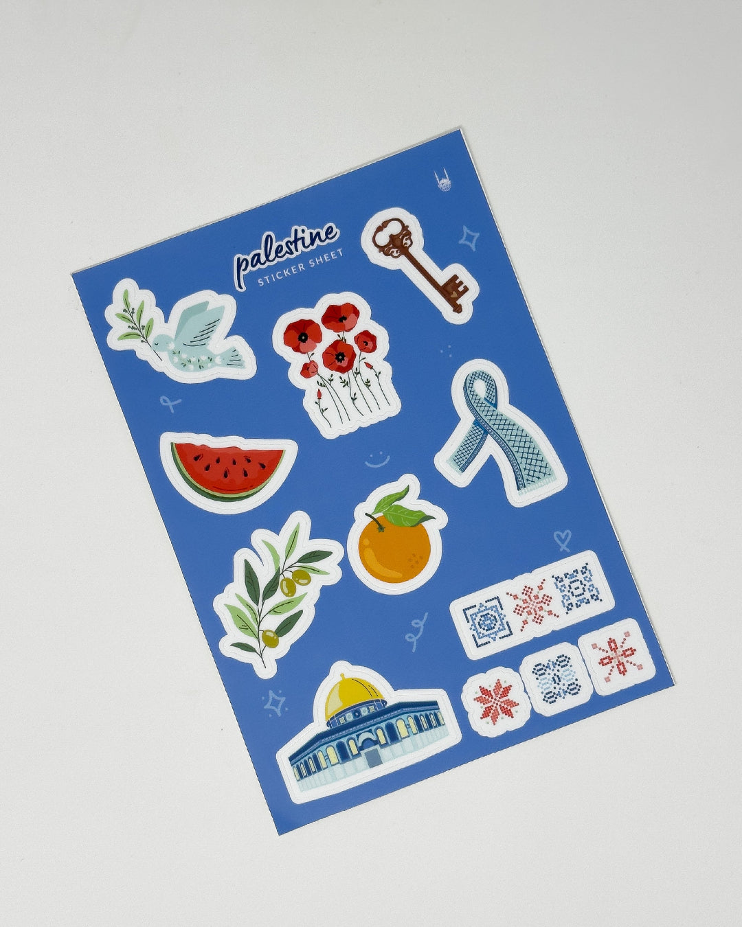 A blue sticker sheet with designs inspired by Palestine, including a dove holding an olive branch, poppies, a key, keffiyeh (scarf), slice of a watermelon, olive branch, jaffa orange, Al-Aqsa mosque and tartreez prints.
