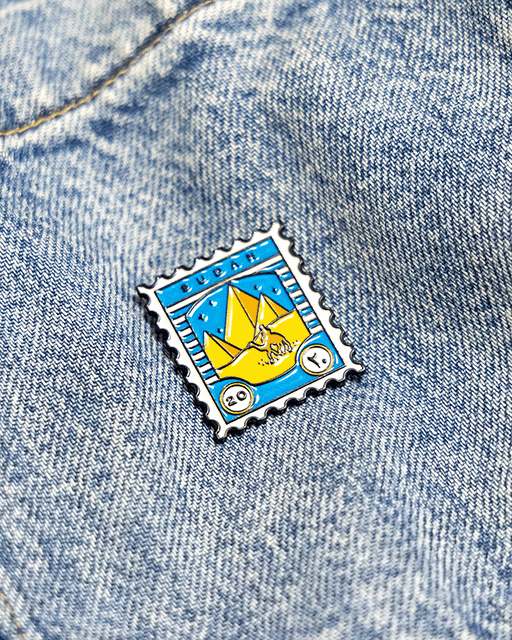 Pin with a design resembling a postage stamp on a denim background inspired by sudanese culture on a brown bag as part of islamic relief uk new sudan souq collection