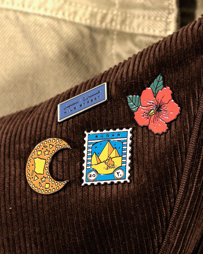 Collection of enamel pin badges inspired by sudanese culture on a brown bag as part of islamic relief uk new sudan souq collection