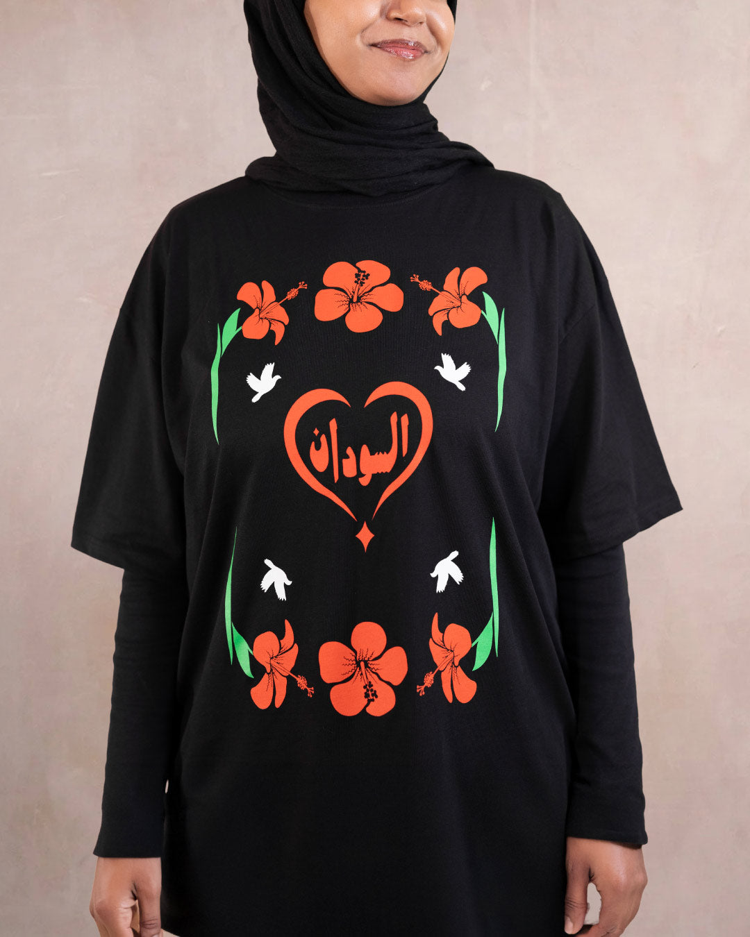 Woman wearing a black t-shirt with red hibiscus flower, white doves and heart design inspired by sudanese culture on a brown bag as part of islamic relief uk new sudan souq collection