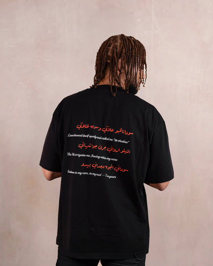 Back of man wearing a black t-shirt with red hibiscus flower, white doves and heart design inspired by sudanese culture on a brown bag as part of islamic relief uk new sudan souq collection
