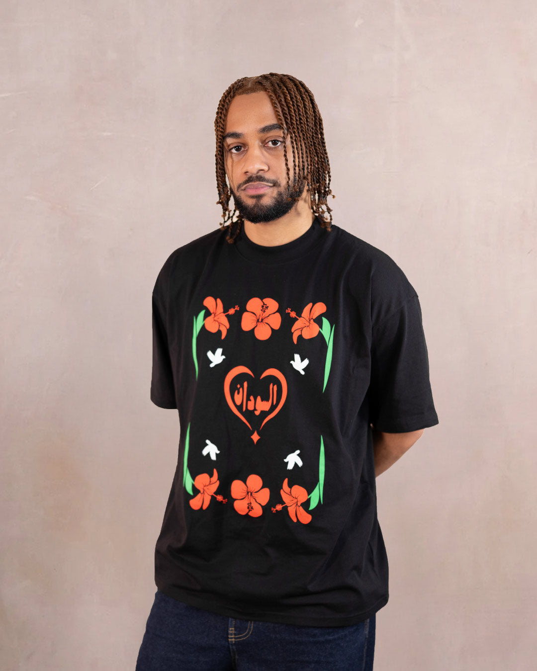 Man wearing a black t-shirt with red hibiscus flower, white doves and heart design inspired by sudanese culture on a brown bag as part of islamic relief uk new sudan souq collection