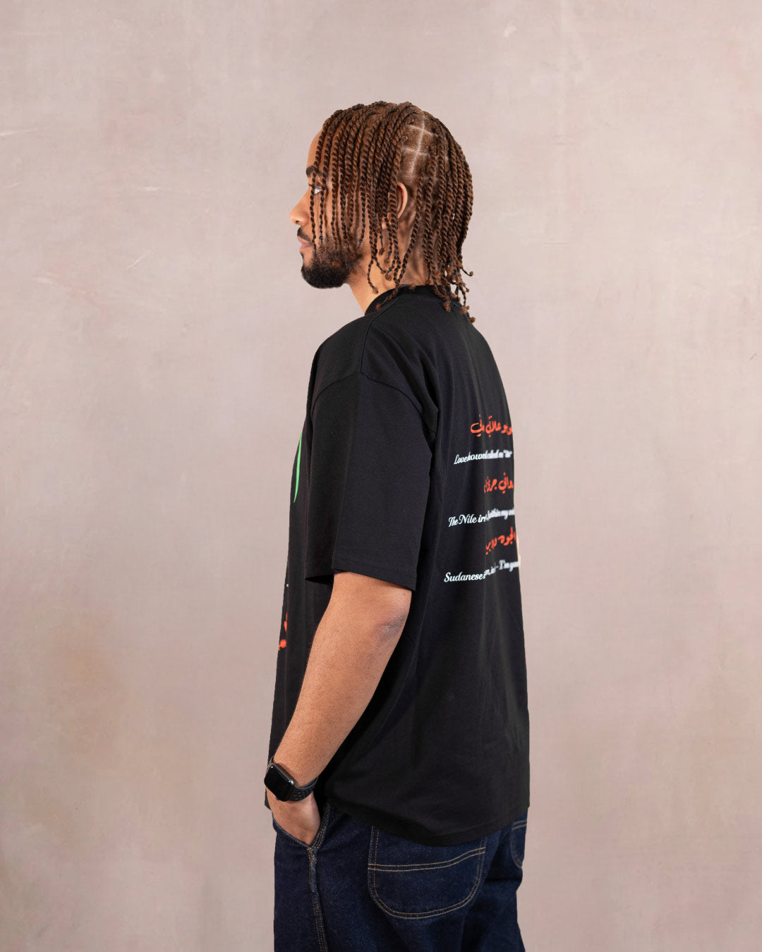 Side profile of man wearing a black t-shirt with red hibiscus flower, white doves and heart design inspired by sudanese culture on a brown bag as part of islamic relief uk new sudan souq collection