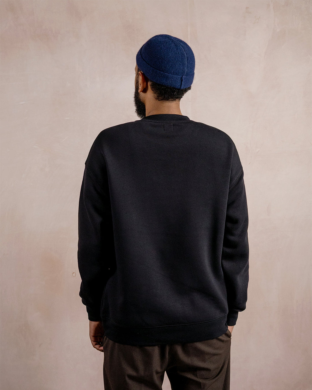 the back of a man wearing a black sweatshirt and blue hat