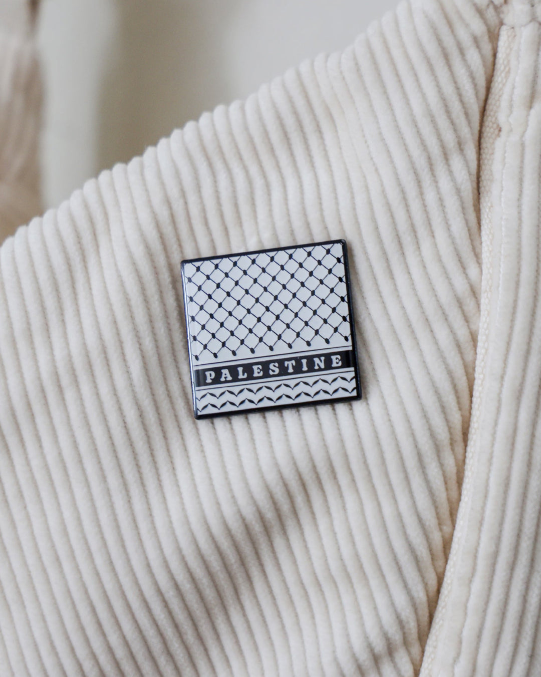 a square pin badge with the keffiyeh prints on it with the word palestine written on it