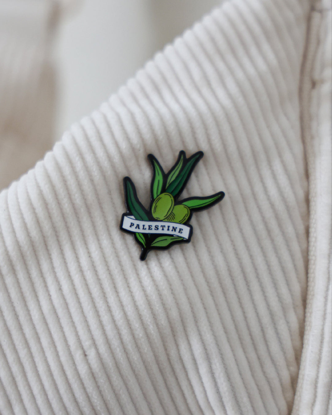 a pin badge of an olive branch with a ribbon wrapped around it with palestine written on it