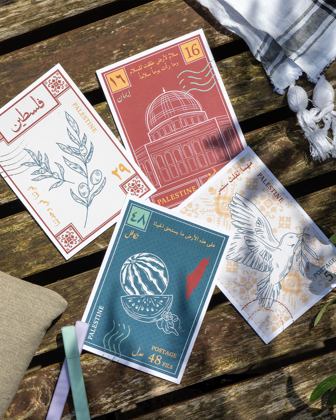 Four postcards with designs inspired by palestinian culture on a wooden bench