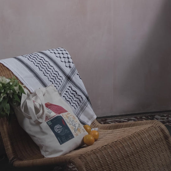 A stop motion clip of a woman adding oranges to a tote bag with a design inspired by palestinian culture and white flowers inside, with a black and white palestinian keffiyeh resting on the chair