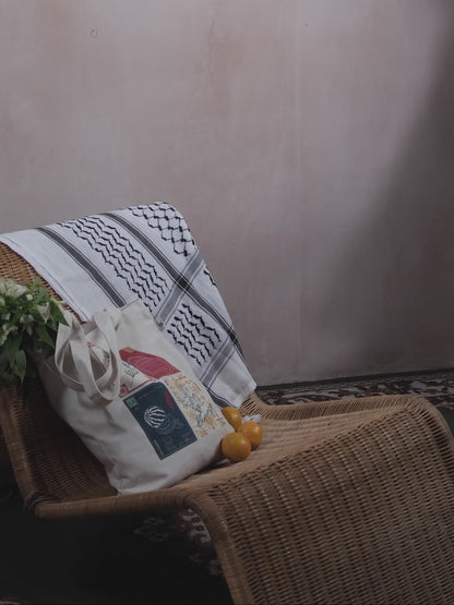 A stop motion clip of a woman adding oranges to a tote bag with a design inspired by palestinian culture and white flowers inside, with a black and white palestinian keffiyeh resting on the chair