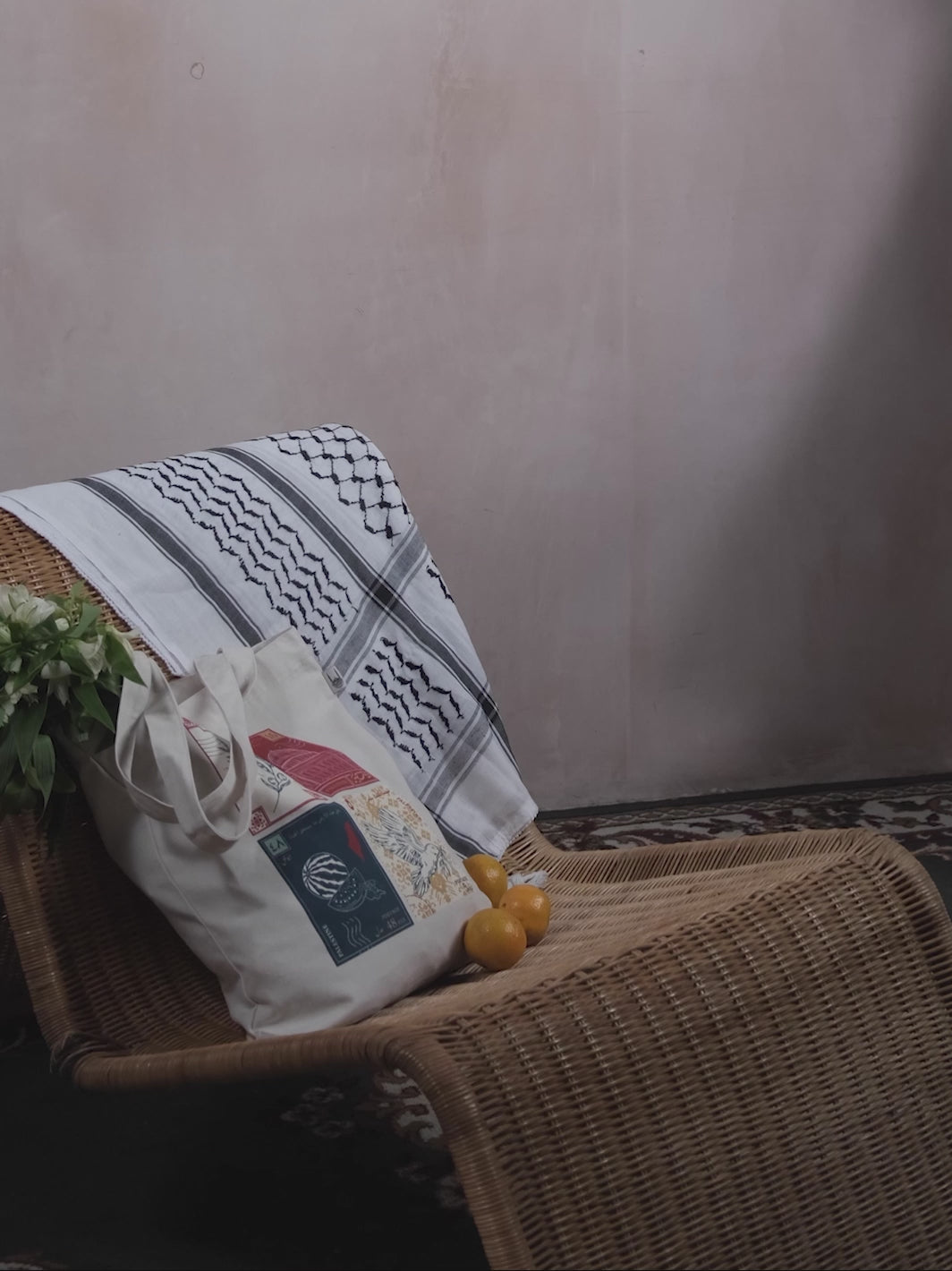 A stop motion clip of a woman adding oranges to a tote bag with a design inspired by palestinian culture and white flowers inside, with a black and white palestinian keffiyeh resting on the chair