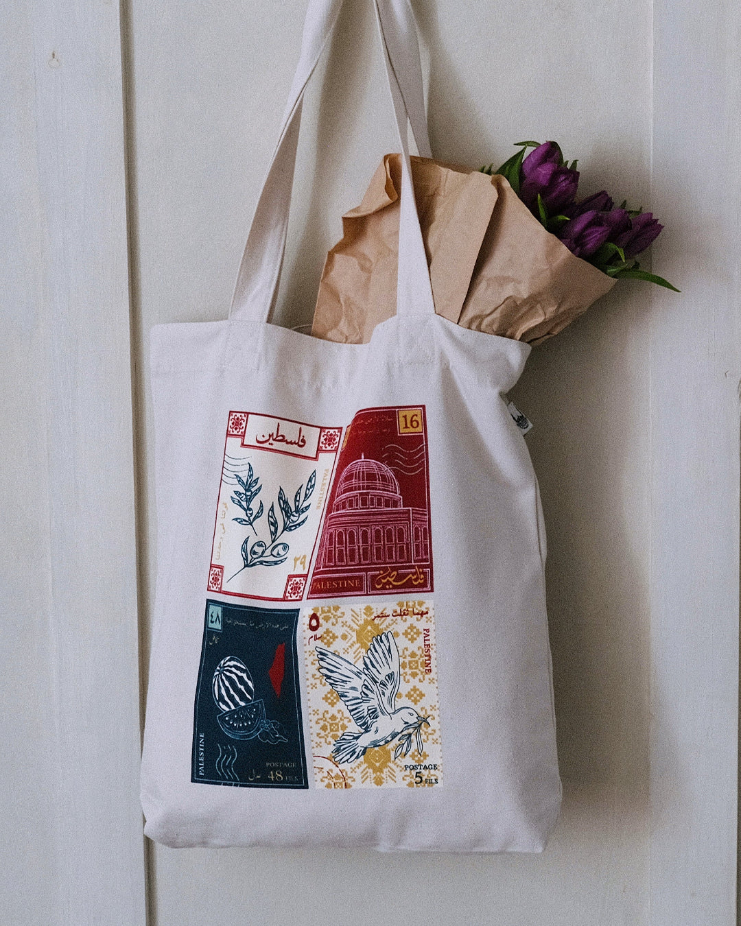 a tote bag with a design inspired by palestinian culture hanging with purple flowers inside
