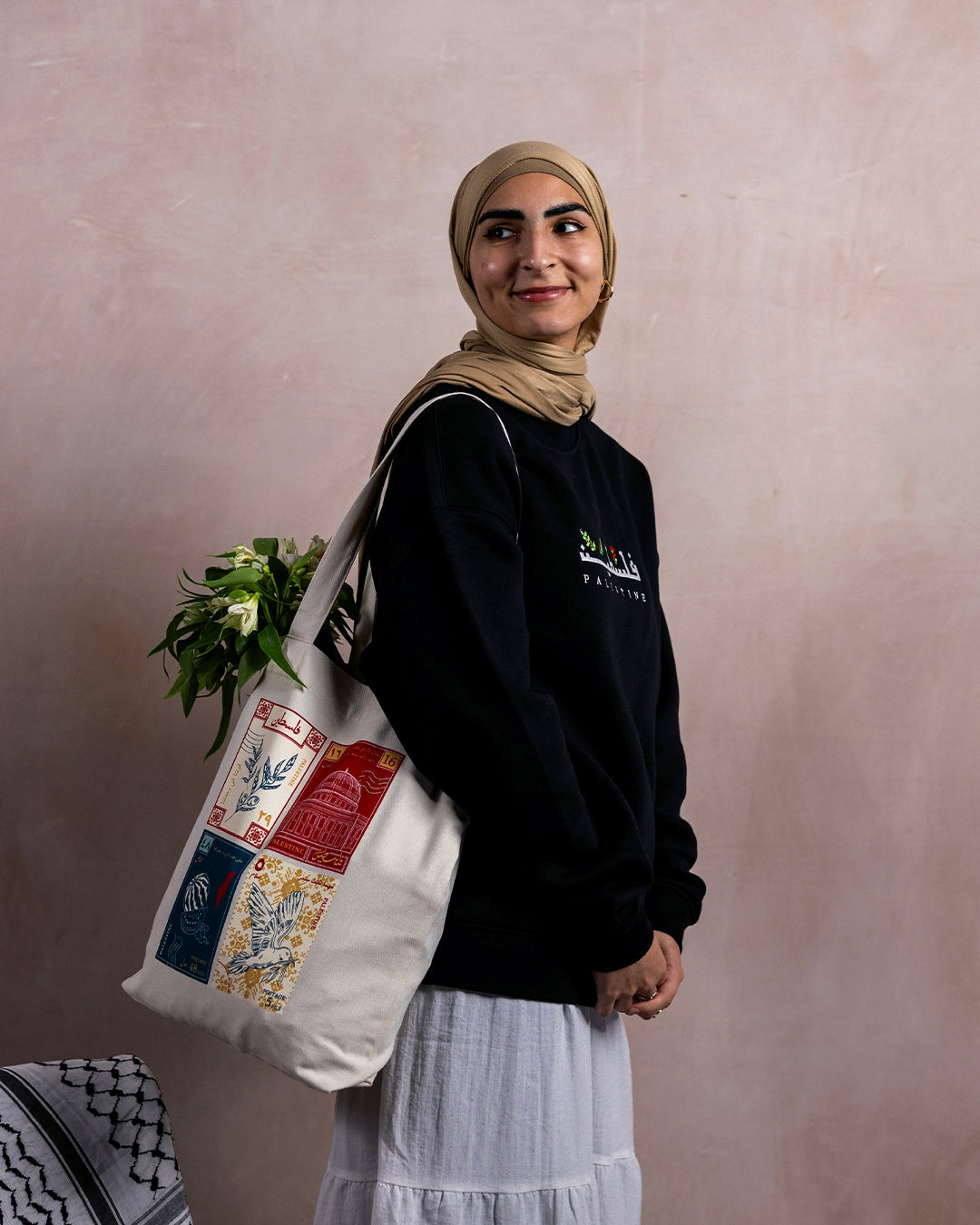 a female wearing a tote bag with a design inspired by palestinian culture hanging with white flowers inside